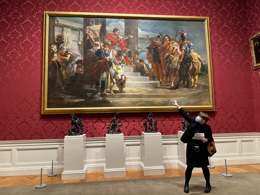 A tour guide standing in front of (and gesturing at) a giant 18th-century painting on the wall of the Walters Art Museum.